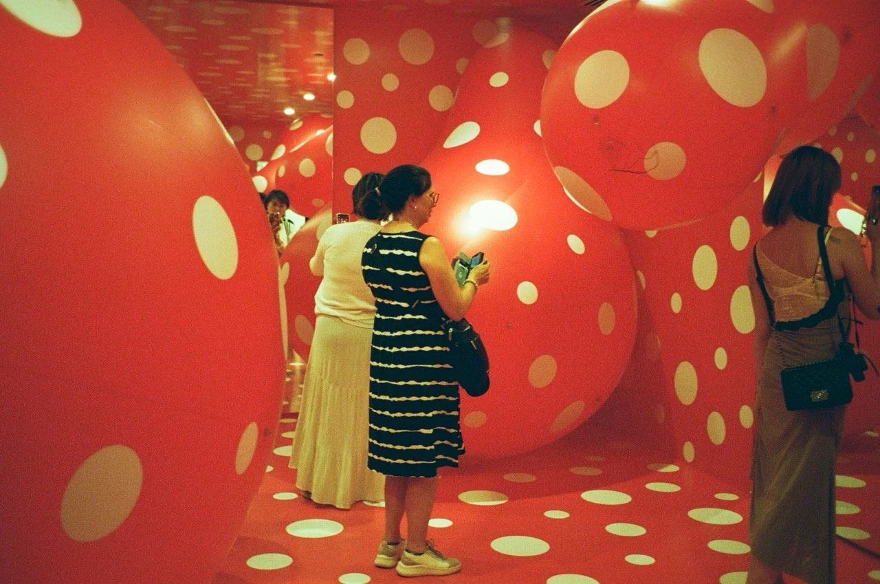 People inside an art installation with large, irregular red walls and floors covered in white polka dots.