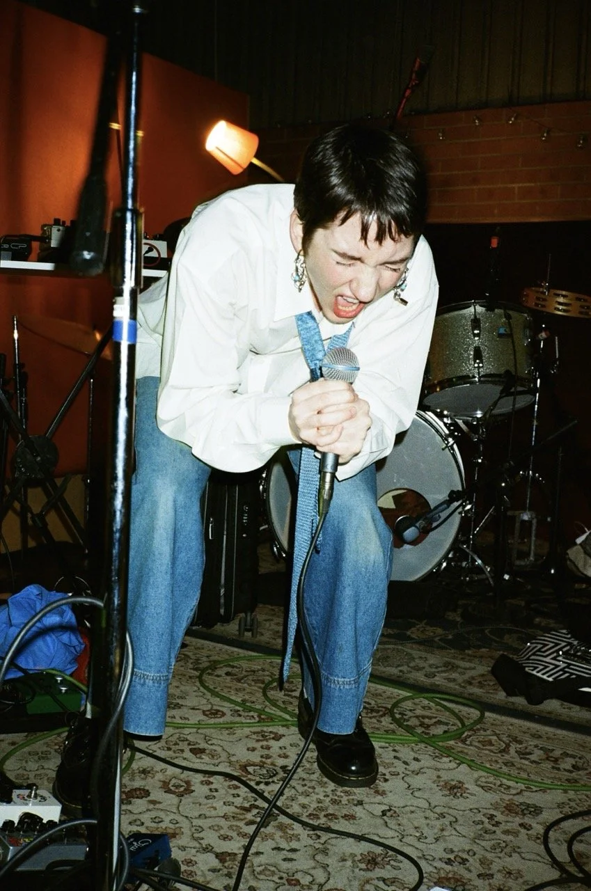 A woman passionately singing into a microphone on a stage with musical instruments in the background.