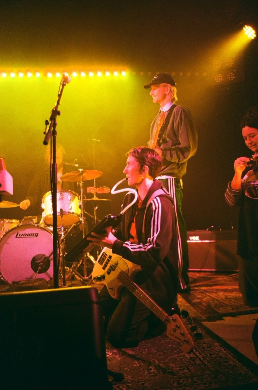 Musicians performing on stage with guitars, drums, and a microphone, illuminated by colorful stage lights.