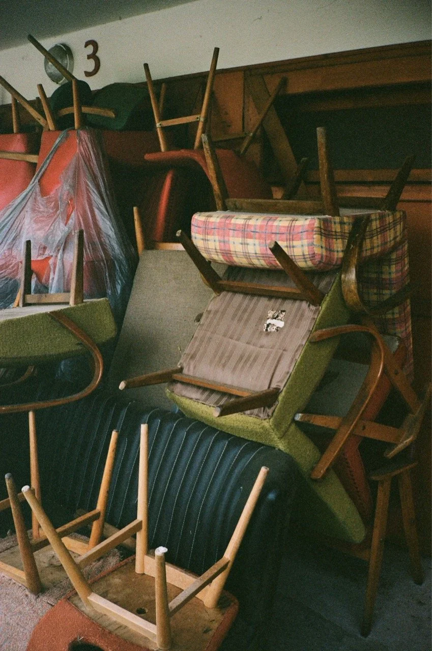 Pile of stacked chairs and tables upside down in a cluttered space.