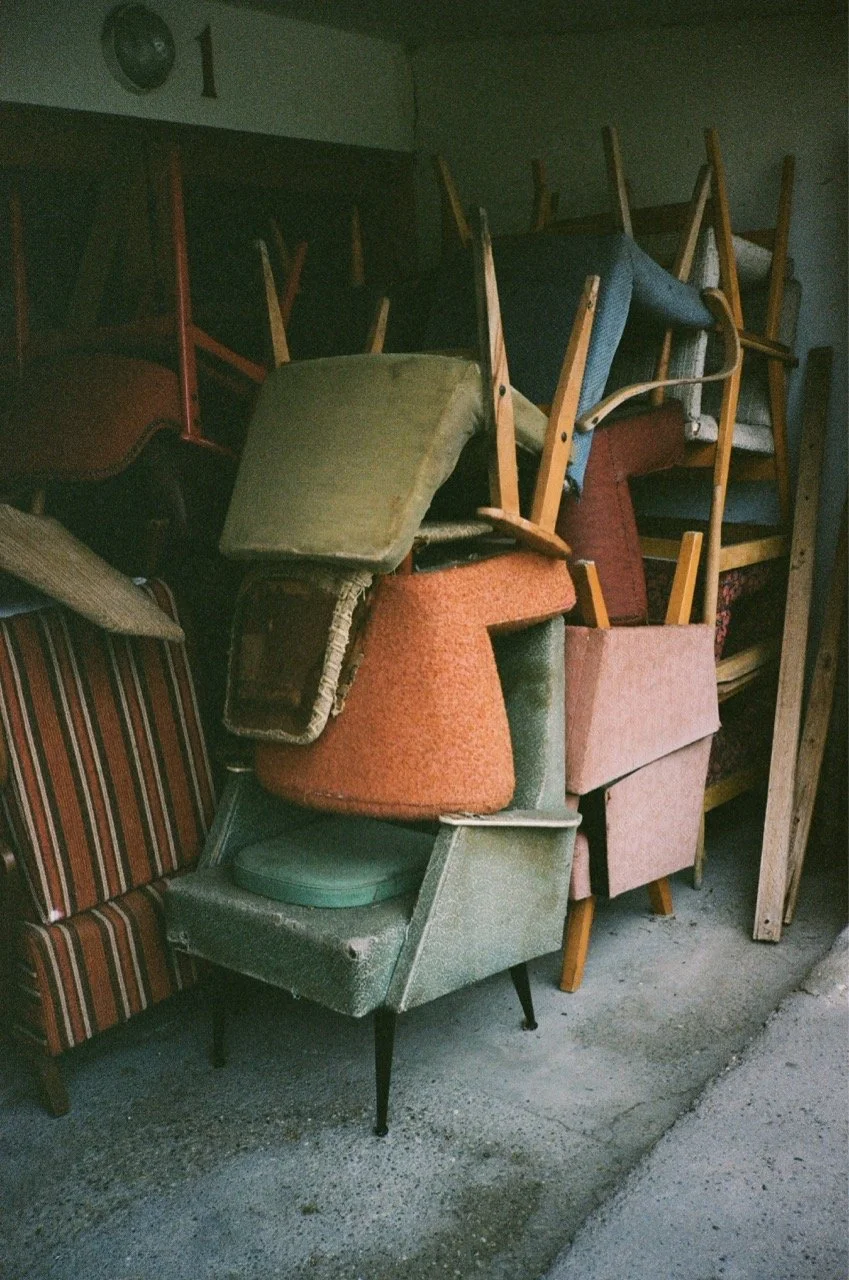 Pile of used and refurbished chairs and furniture stacked in a storage area.