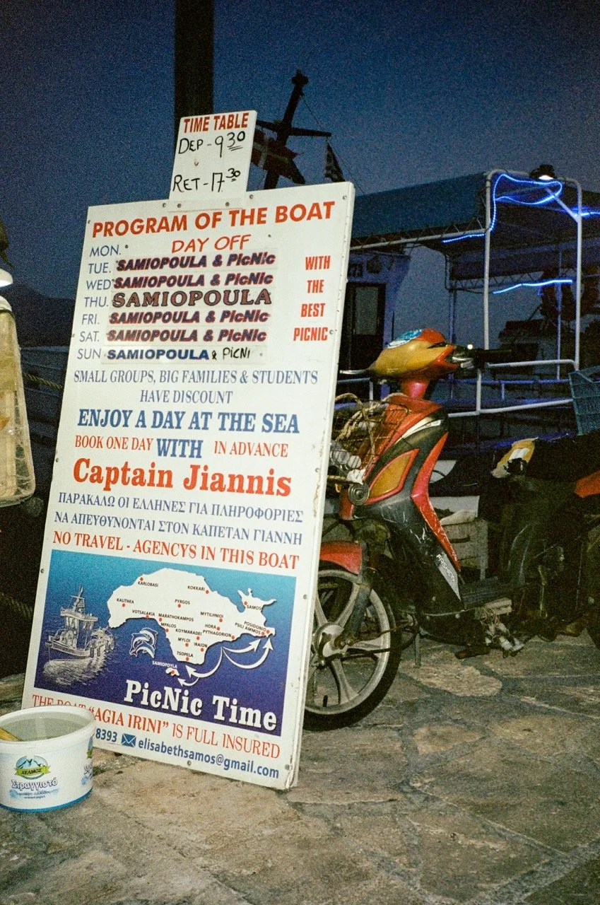 Signboard with boat schedules and program details next to a scooter and a small part of a boat deck at dusk or evening.