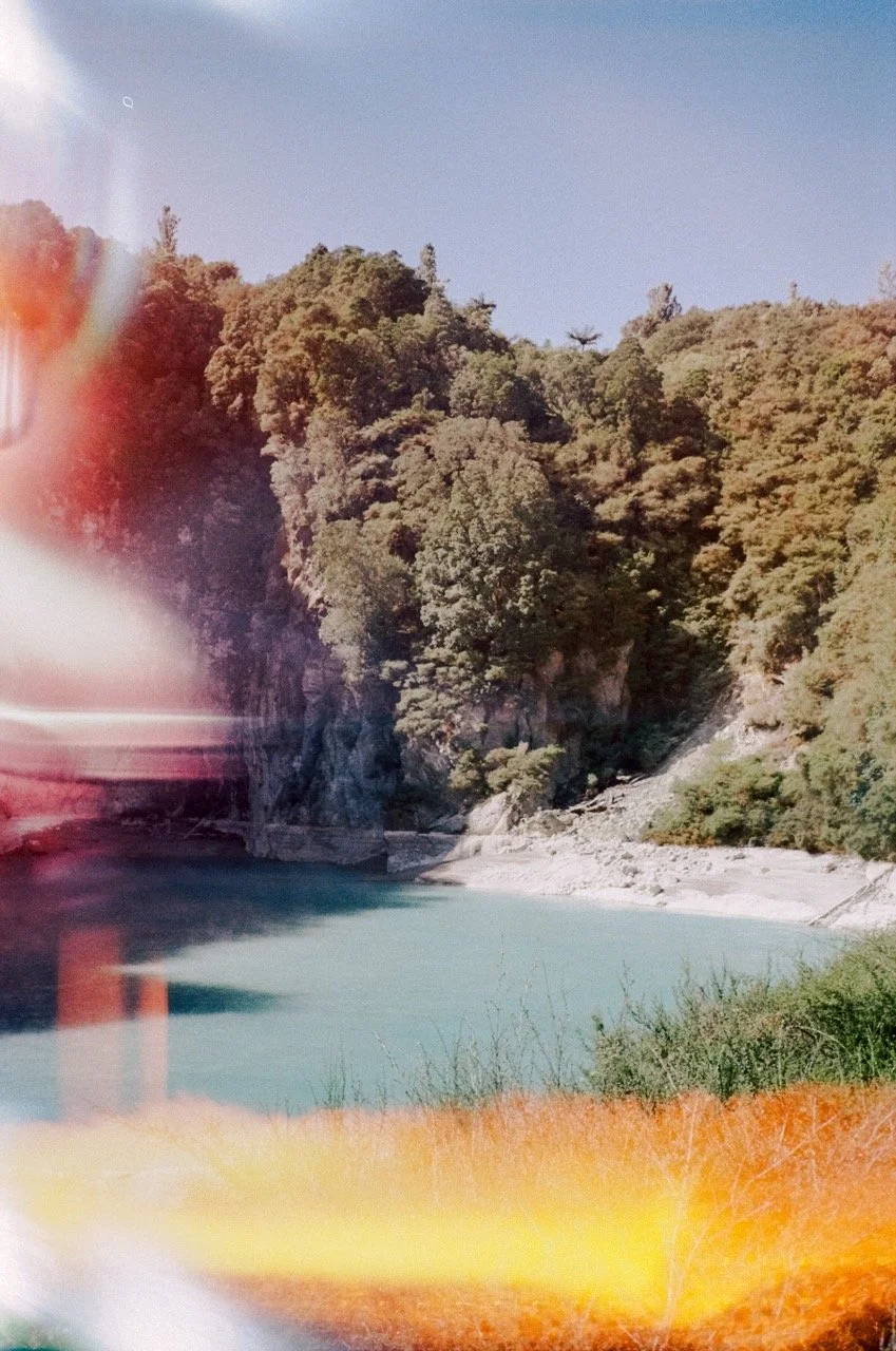 A scenic view of a river surrounded by lush green trees and rocky hills under a clear blue sky.