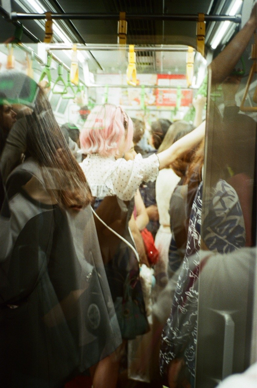 People standing close together inside a crowded train or subway car, holding onto handrails.