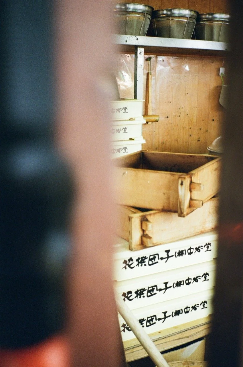 View of a storage area with metal containers on a shelf and stacked boxes with Japanese writing, seen through a partially obstructed view.
