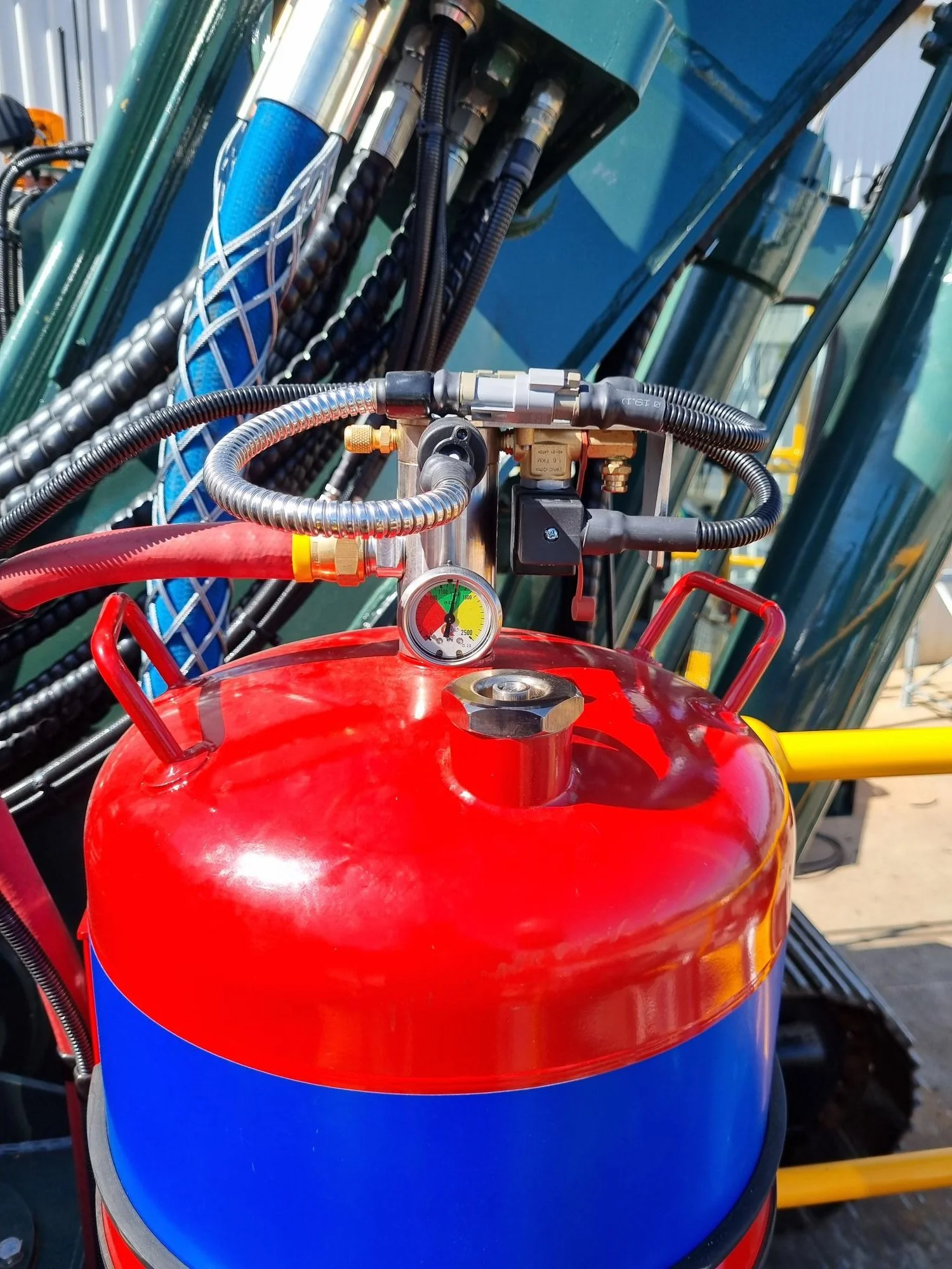 Close-up of construction equipment featuring a red and blue compressed air tank, a pressure gauge, and various hoses and connectors.