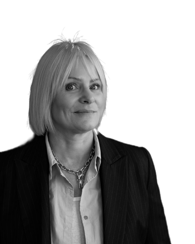 Black and white portrait of a woman with short blonde hair wearing a dark pinstripe blazer, a white shirt, and a chunky chain necklace.
