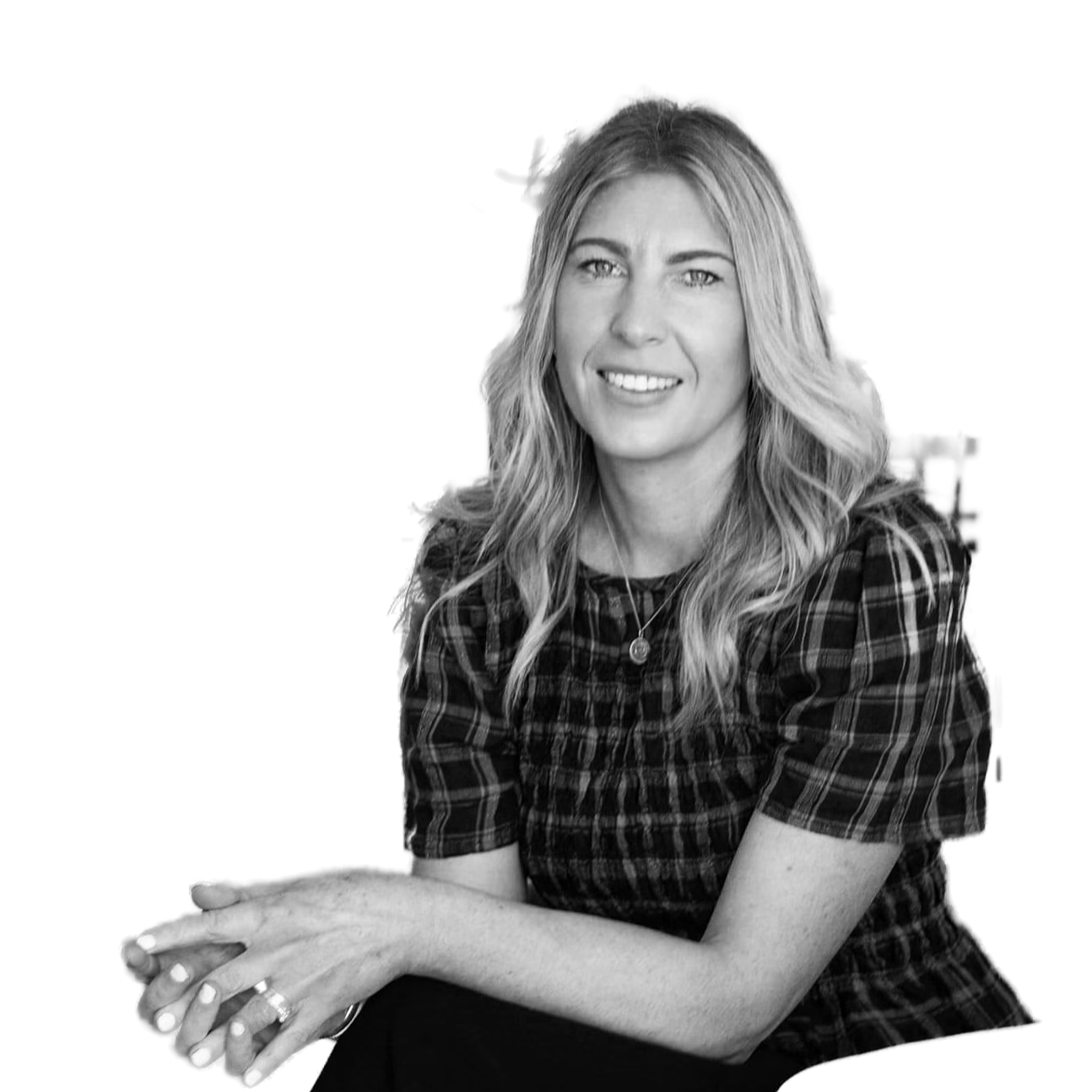 Black and white photograph of a woman with wavy blonde hair, smiling, wearing a checkered top, sitting with her hands clasped.