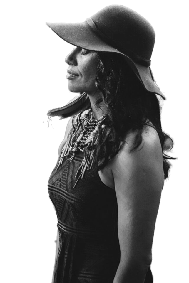 Black and white photograph of a woman wearing a wide-brimmed hat, with dark, wavy hair, and layers of necklaces. She is looking to the side with a calm expression.