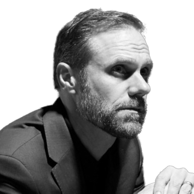 Black and white portrait of a man with a beard and short hair, looking to the side with a serious expression.