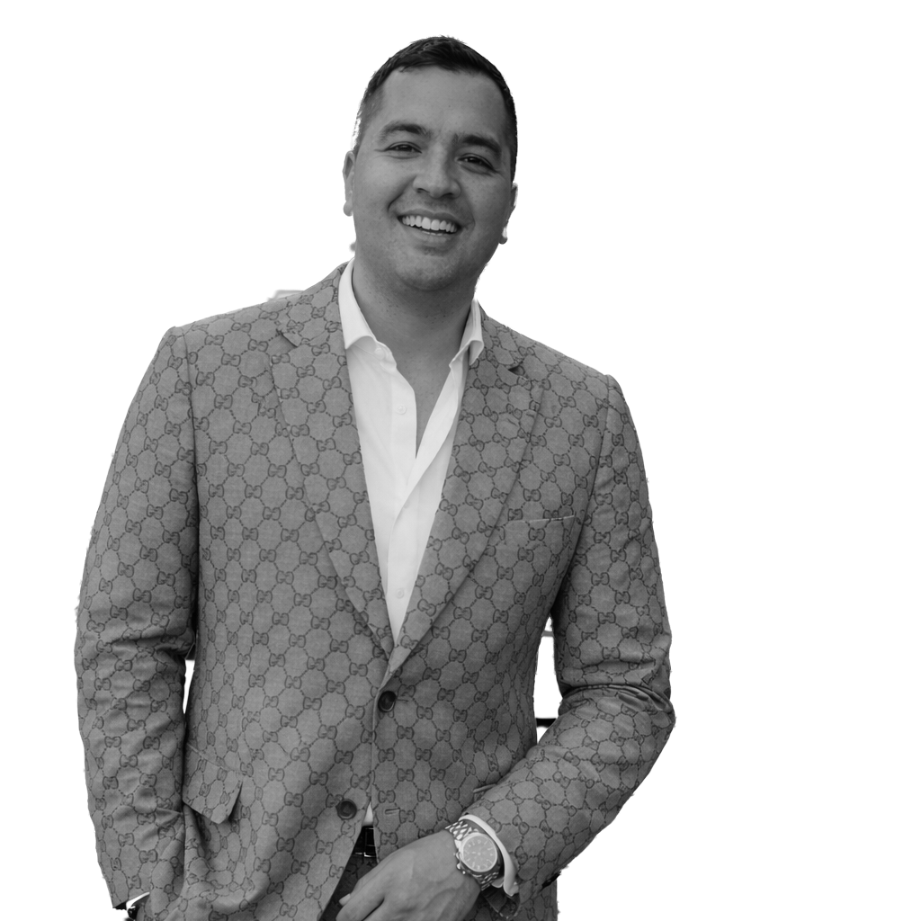 A smiling man in a patterned blazer, white shirt, and watch posing against a plain background.