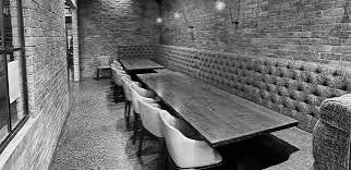 A long wooden dining table with chairs and a cushioned bench along the wall in a brick-walled restaurant or cafe.