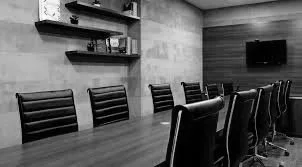 A conference room with a long wooden table and eight black leather chairs, a wall-mounted TV, and shelves with decorative items.