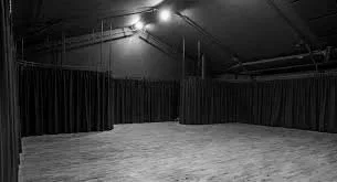 Empty dance studio with wooden flooring, dark curtains, and string lights hanging from the ceiling.
