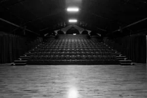 Empty theater stage with seats and steps leading up to the stage, in black and white.