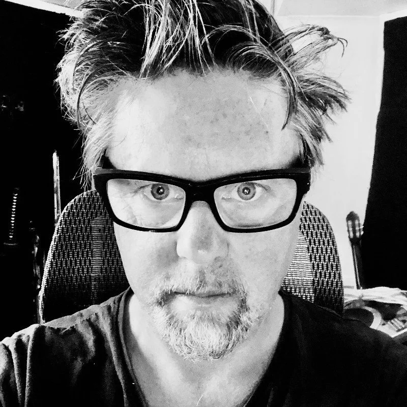 A man with glasses and a beard looking directly at the camera in a black-and-white photo.