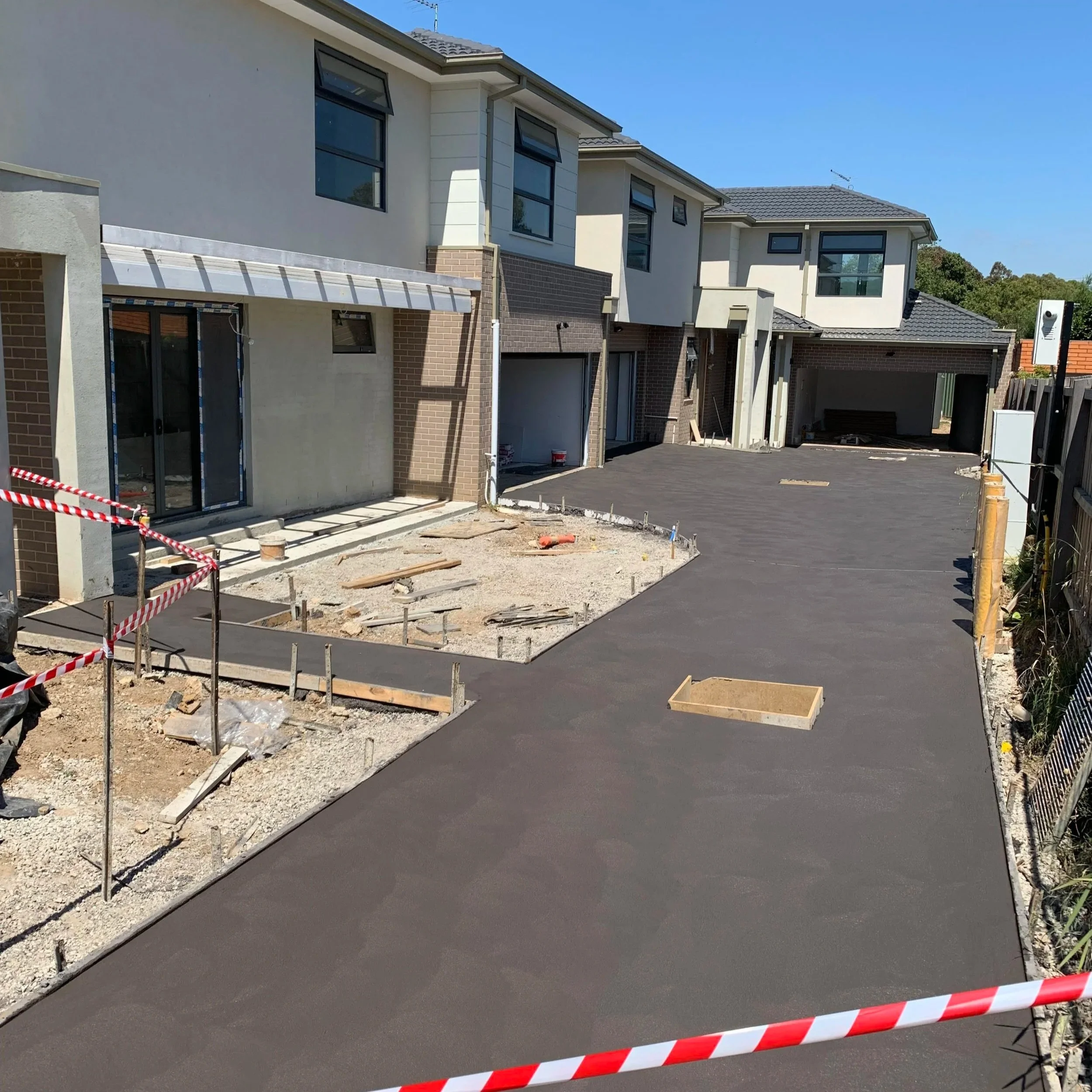 Under construction of a new residential building with a paved driveway and unfinished yard, blue sky, and neighboring houses.