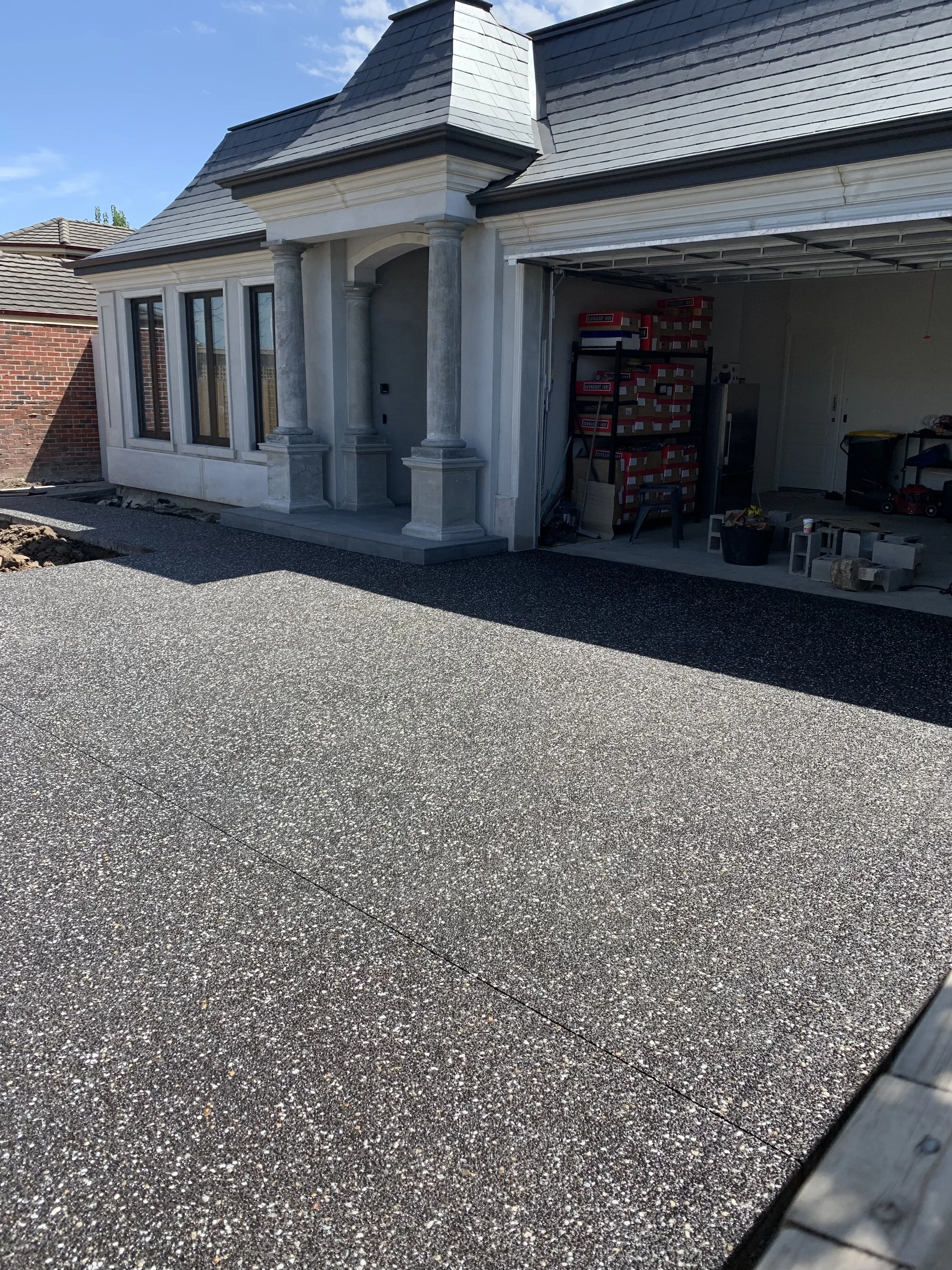Newly paved driveway in front of a house with a garage under construction or renovation, showing construction materials and tools inside the garage.