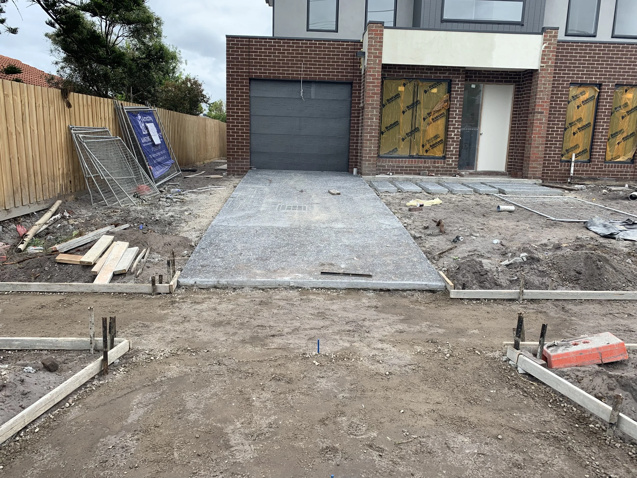 Construction site with a new concrete driveway, unfinished sidewalk, and building under construction in the background.