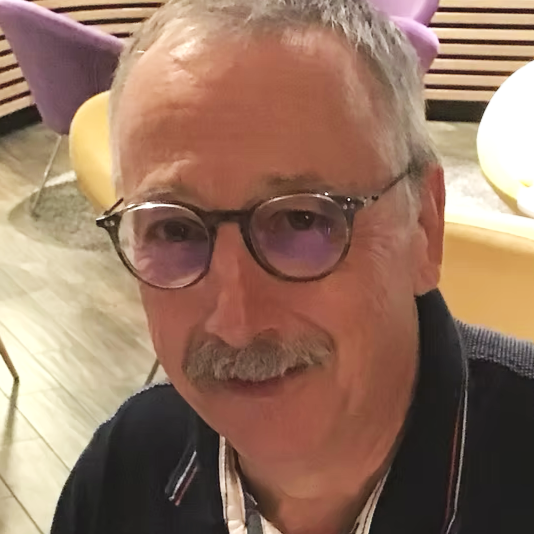 Un homme âgé avec des lunettes rieu à côté d'une décoration de fête colorée.