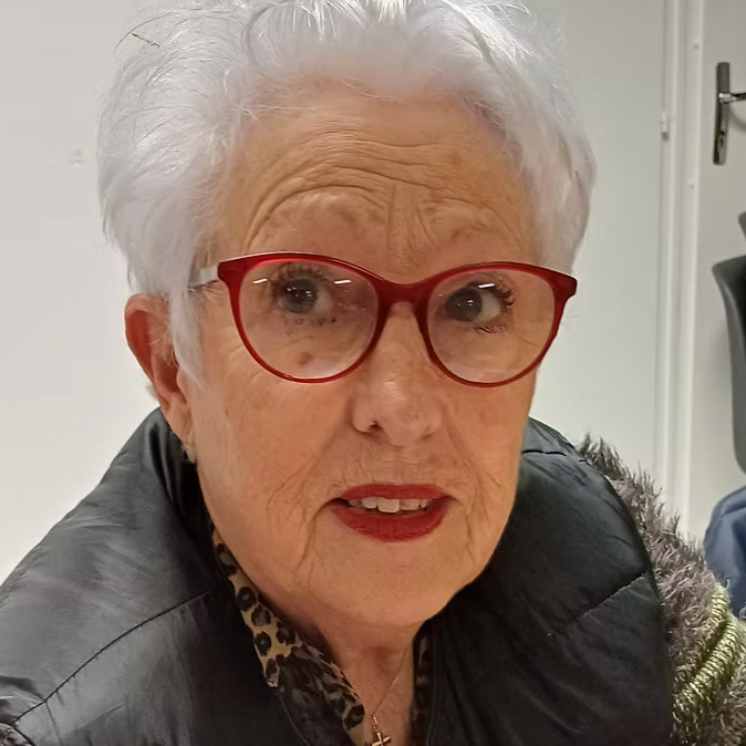 Une femme âgée portant des lunettes rouges et une veste noire, avec des cheveux blancs et courts.