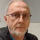 Un portrait d'homme à lunettes, avec des cheveux gris et une barbe, portant un pull noir