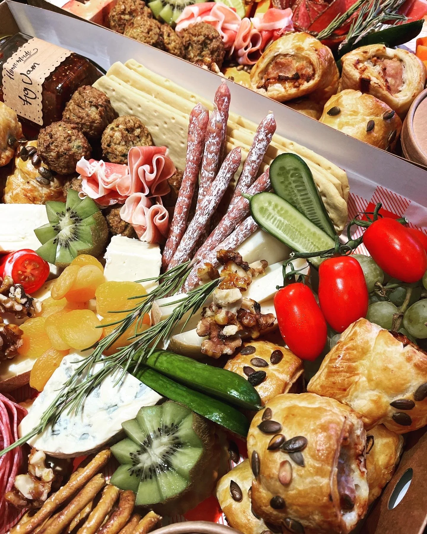 Large Graze Boxes including signature homemade sausage and fennel rolls, cheese slices, cherry tomatoes, cucumber slices, kiwi slices, crackers, fresh herbs, and homemade chutney