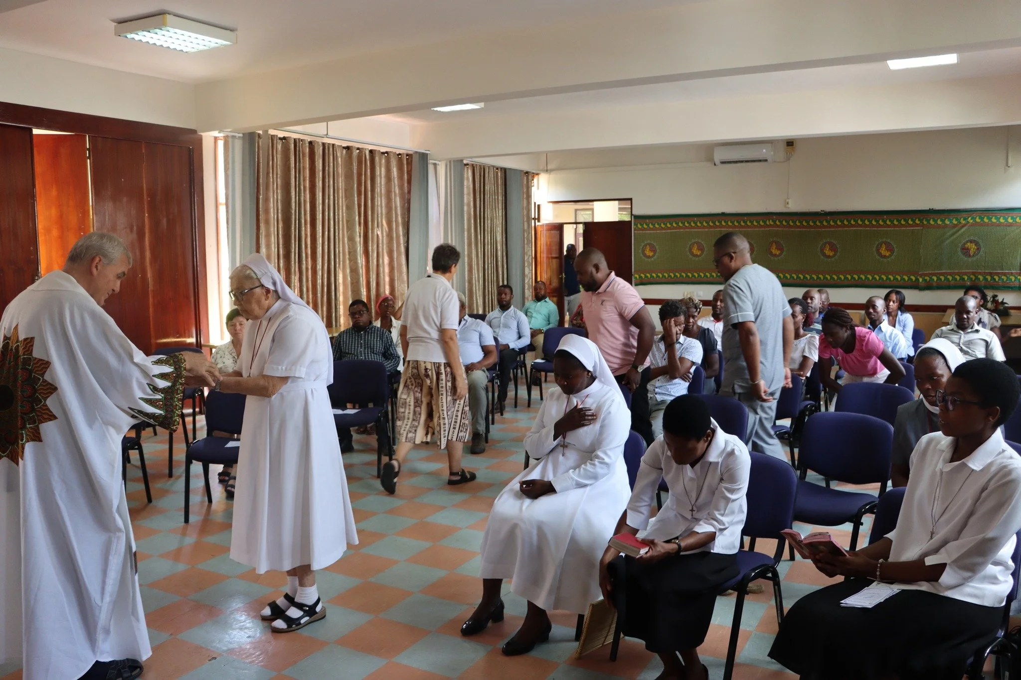 A religious ceremony with priests, nuns, and congregation members in a church or chapel, some seated and some standing.