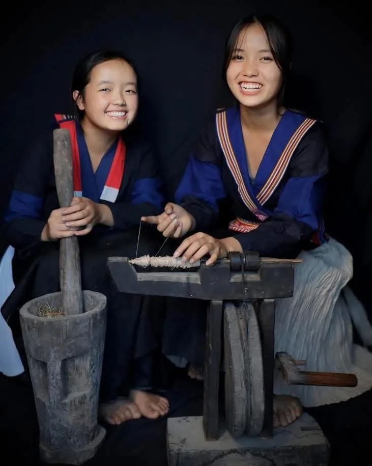 Two Hmong women demonstrating traditional hemp fiber processing using a wooden hand tool before weaving