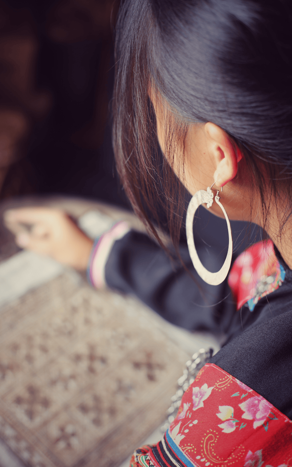 Black view of a Hmong woman wearing traditional indigo clothing and lage silver hoop earings, highlighting cultural dress and identity.