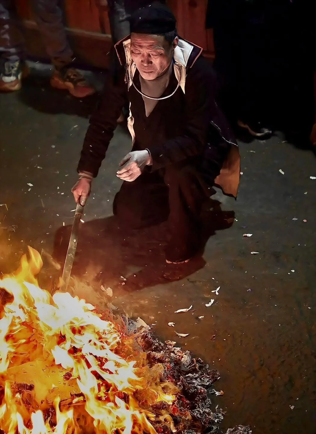 Elder shaman tends a blazing ritual fire with a stick during Hmong New Year rites.