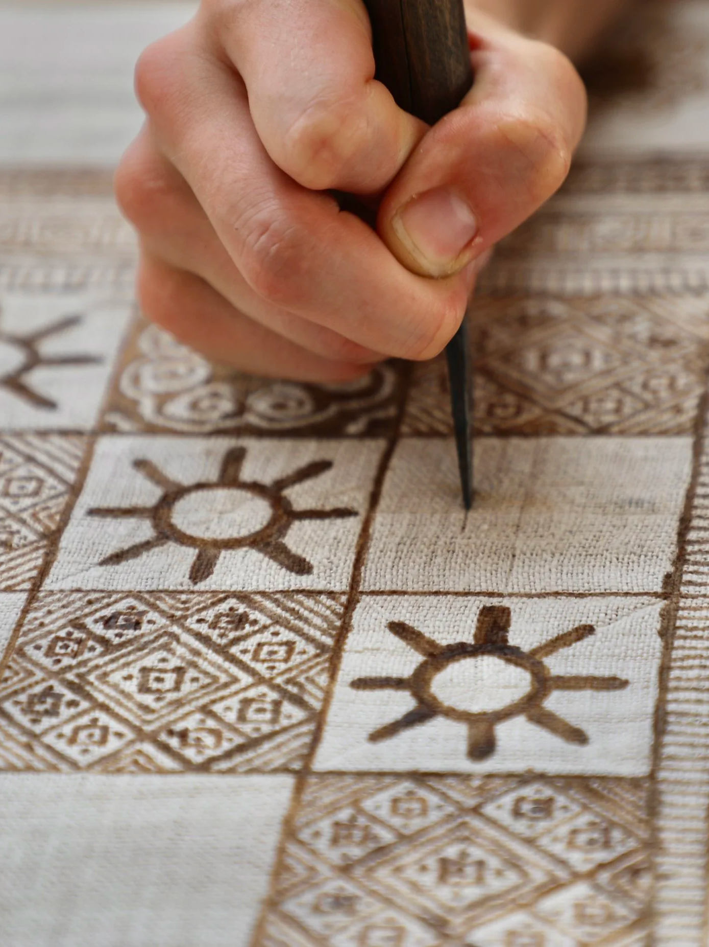 Close-up of batik tool applying wax onto hemp fabric