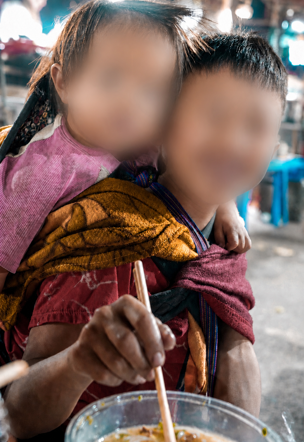 Hmong child carrying a younger child on their back while eating in Sa Pa, with both faces blurred for privacy.