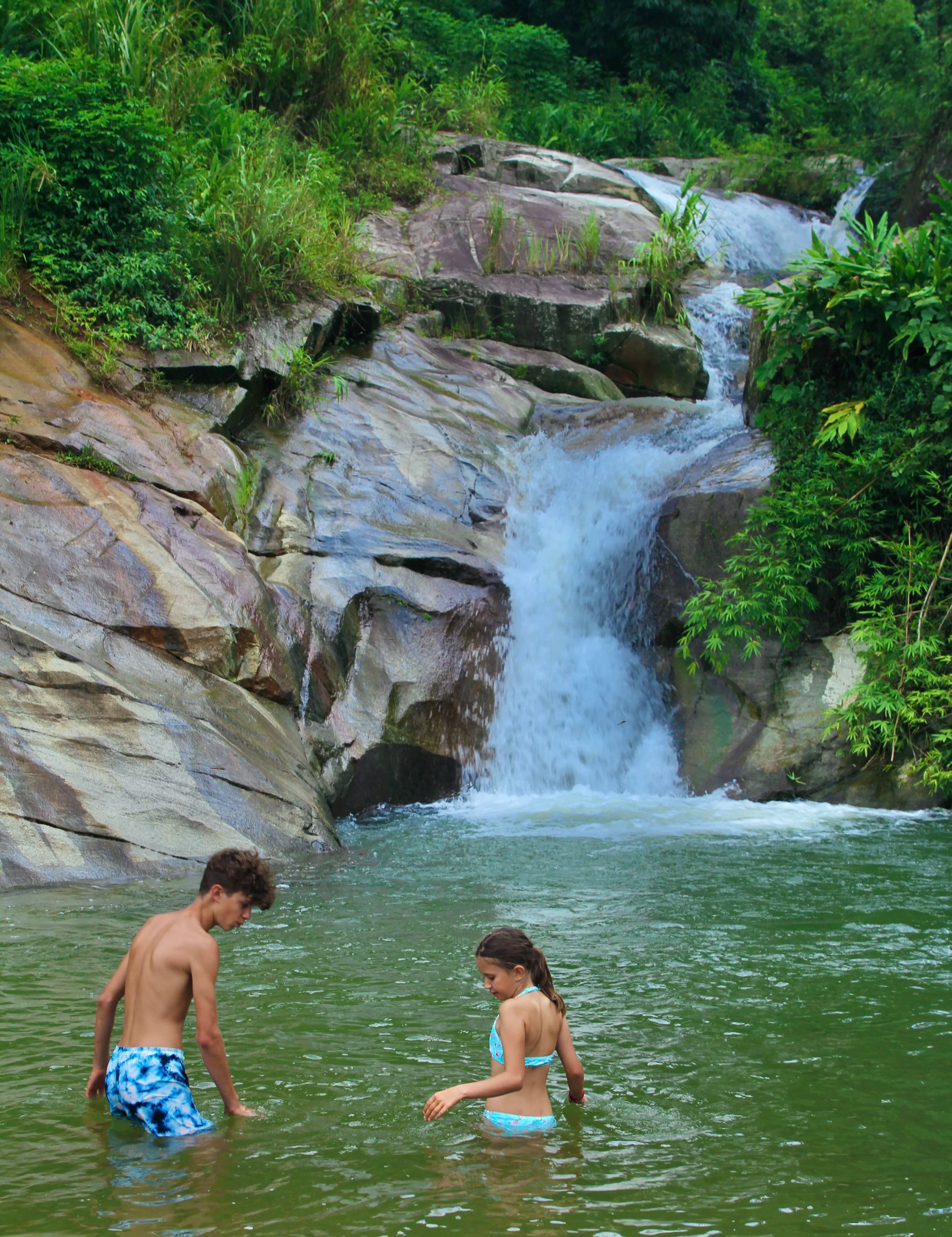 Children playing in natural pool beneath waterfall