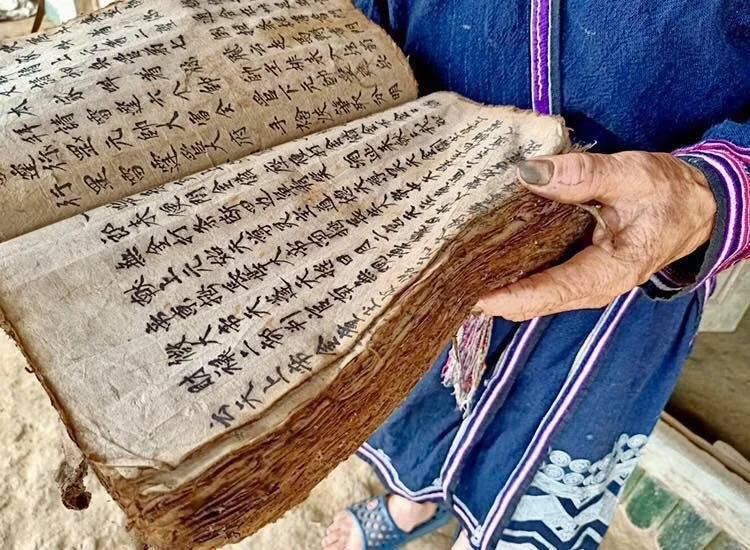 An elderly Red Dao woman carefully holding a well-preserved handwritten family ritual manuscript in Sapa, northern Vietnam.
