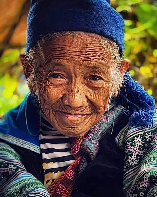 Close portrait of elderly Hmong woman May showing her expressive face and traditional blue head covering.