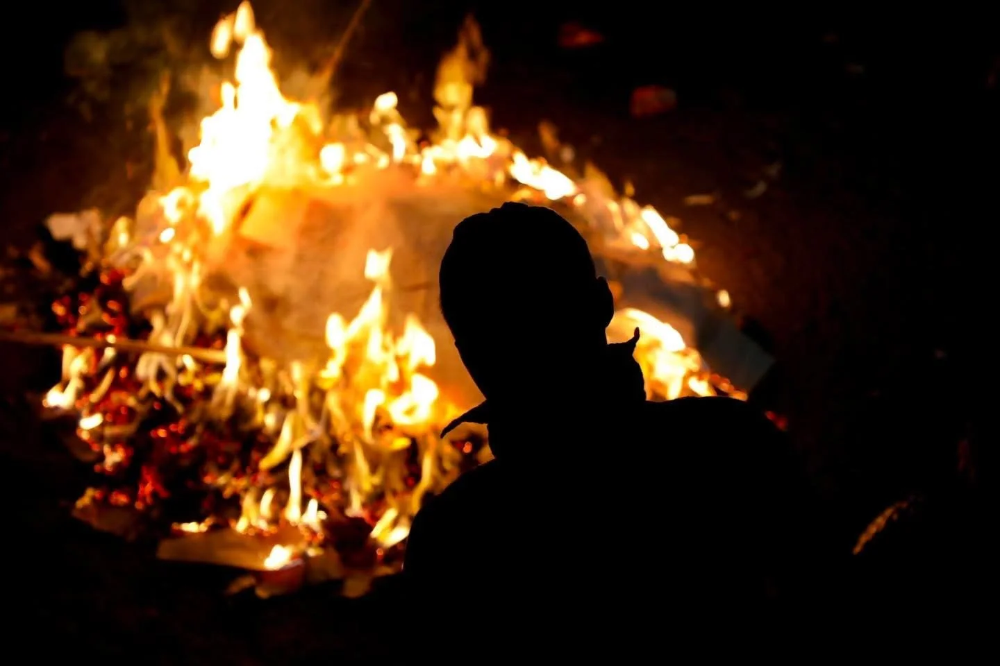 Silhouette of a participant standing by a large bonfire at a Hmong New Year night celebration.