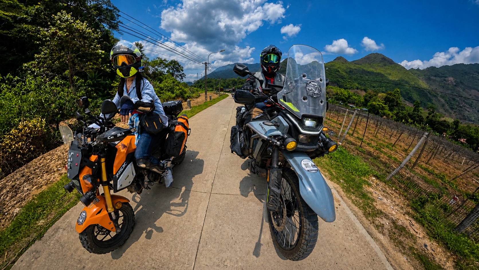 Two motorcyclists riding side by side on a scenic rural road with hills and blue sky.