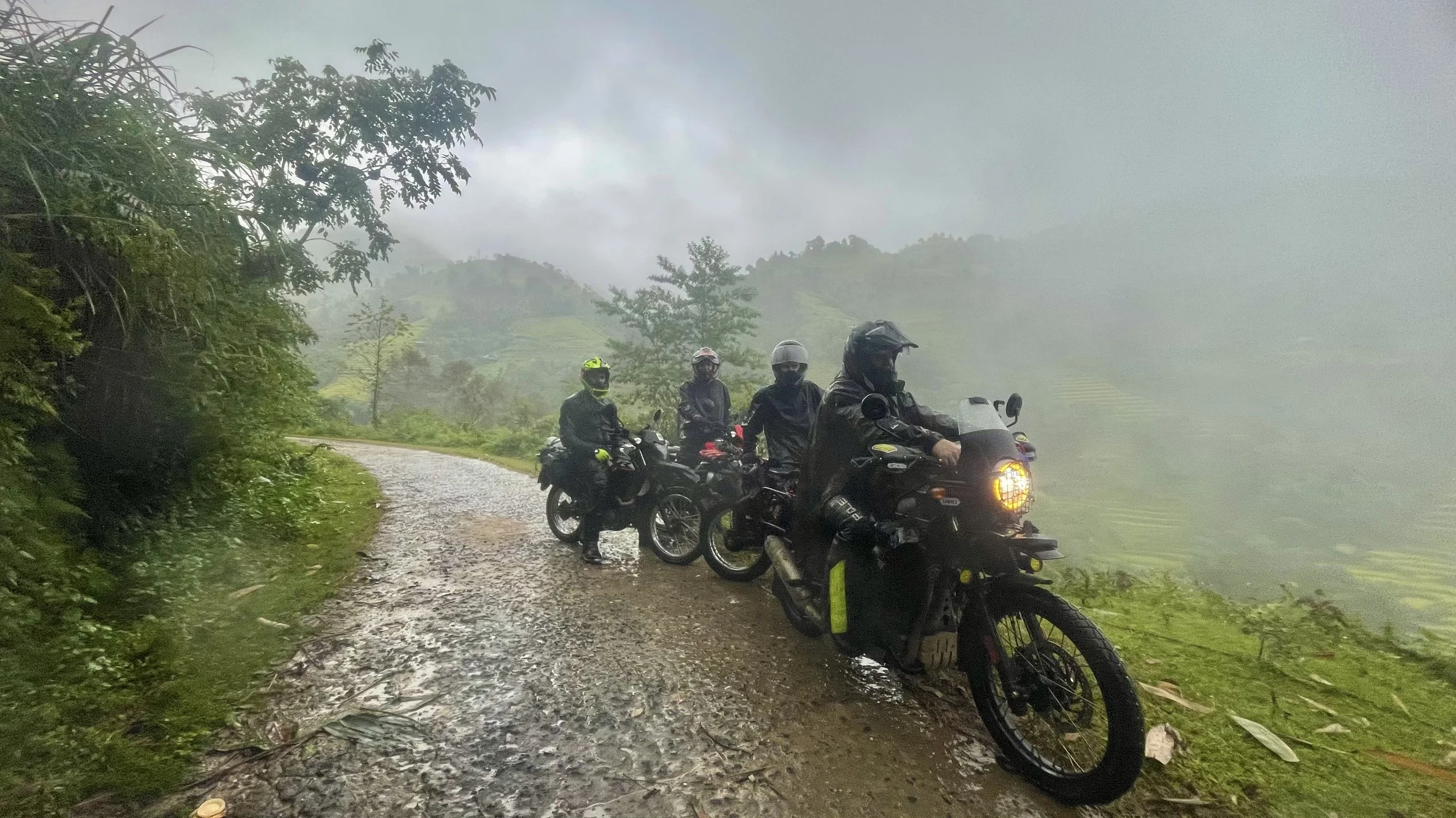 Group of motorbike riders traveling through misty mountain roads during monsoon season on the Ha Giang Loop