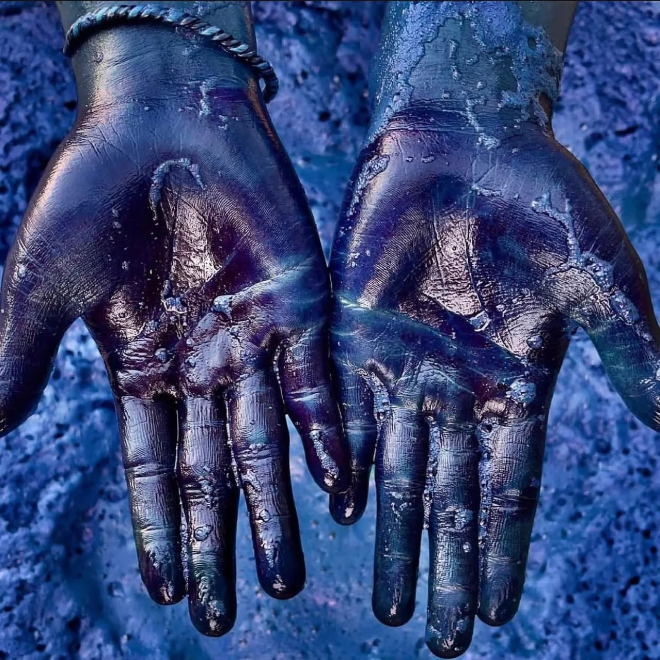 Open palms deeply stained blue from indigo dye, with a twisted metal bracelet around one wrist.