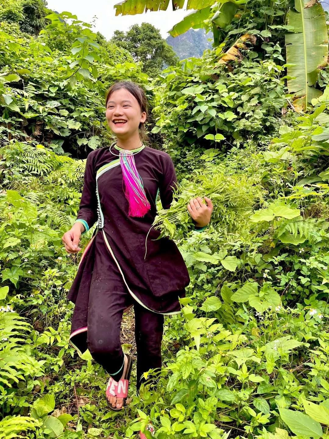 A young Lan Tien girl walking happily through dense green vegetation, wearing traditional clothing in northern Vietnam.