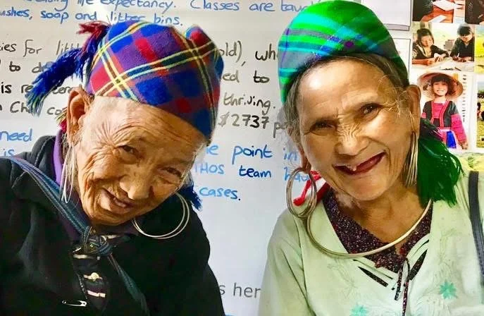 Portrait of elderly Hmong woman May with another woman wearing traditional clothing and a green headscarf.