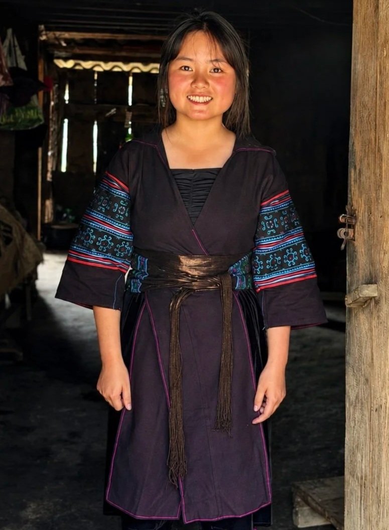 Lý Thị Pằng smiles inside her family home in Pa Cheo while wearing traditional Black Hmong clothing.
