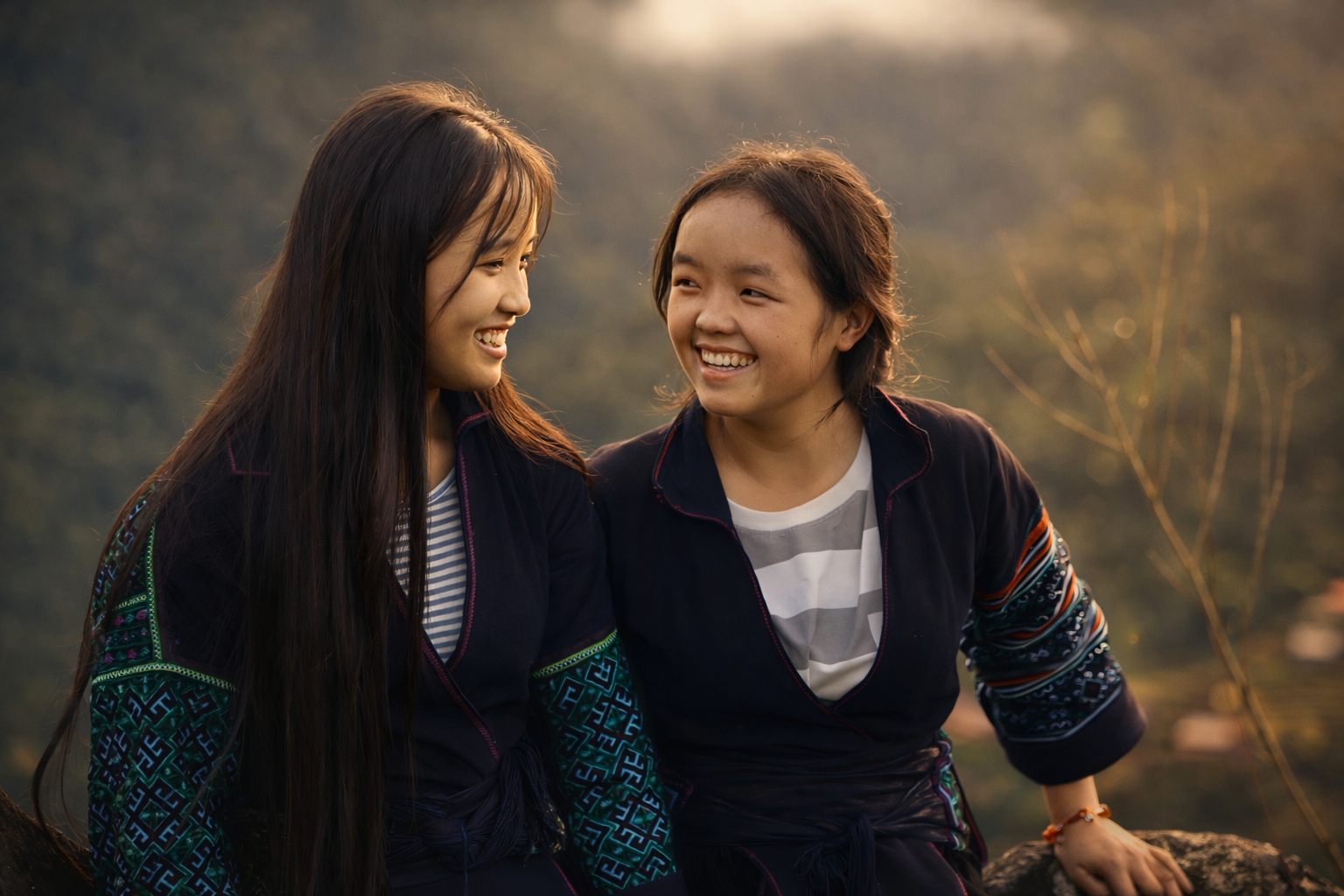 Two young women smiling at each other outdoors during sunset, wearing casual jackets and standing against a blurred natural background.