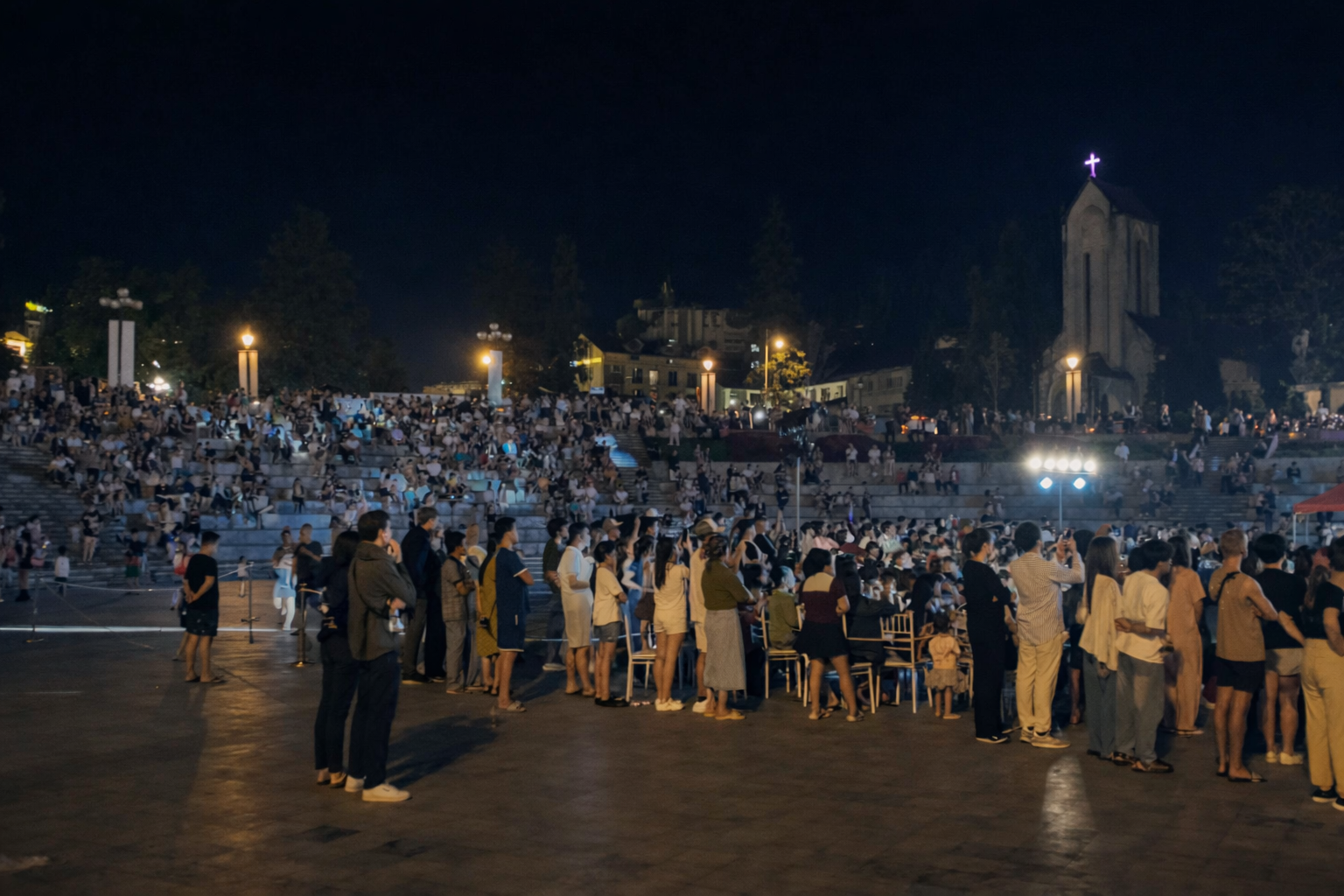 A large crowd gathered in a brightly lit town square at night, showing the busy and social atmosphere of Sapa tourism.