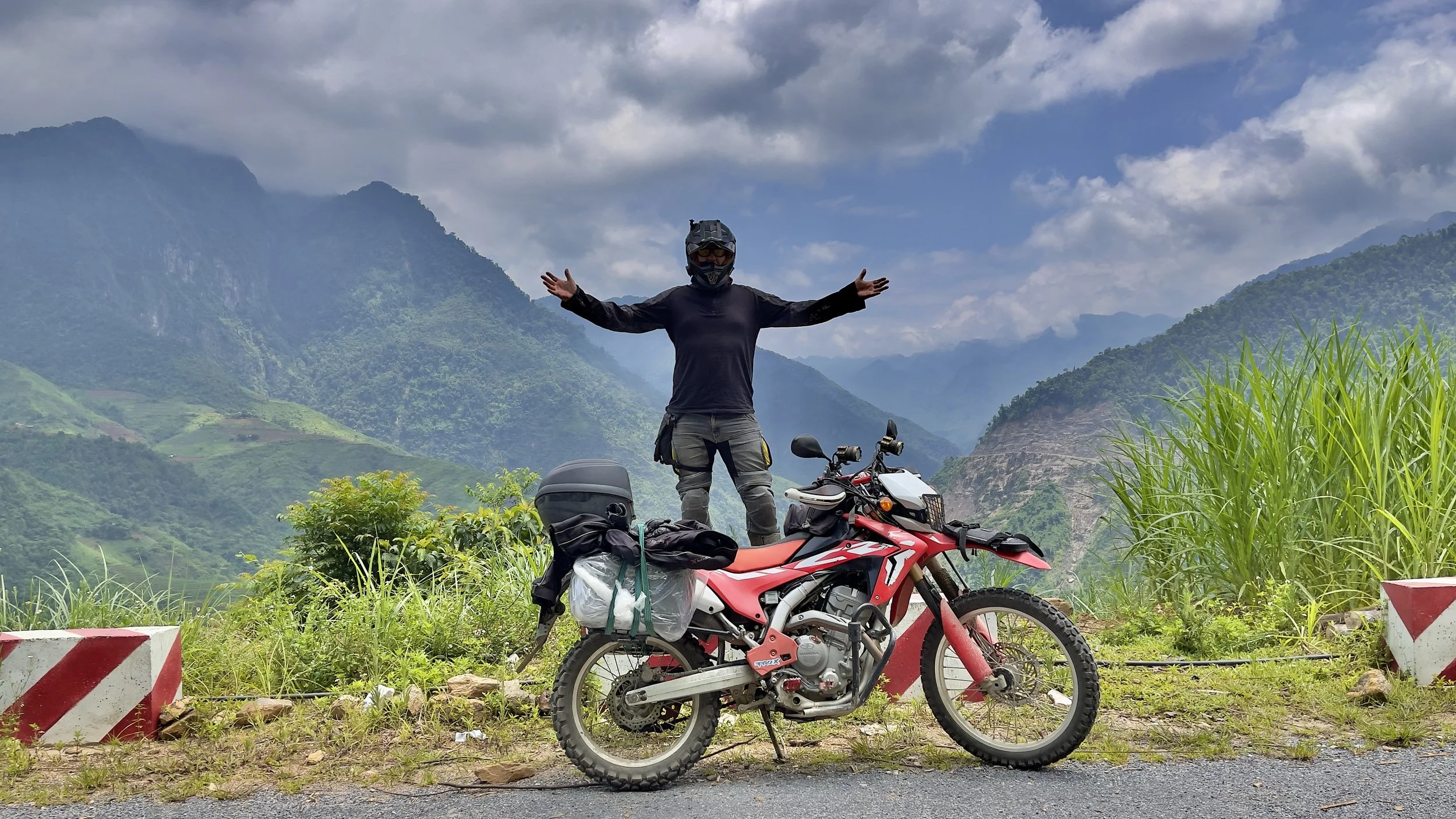 Solo traveller standing beside a motorbike overlooking mountain scenery on the Ha Giang Loop in Vietnam