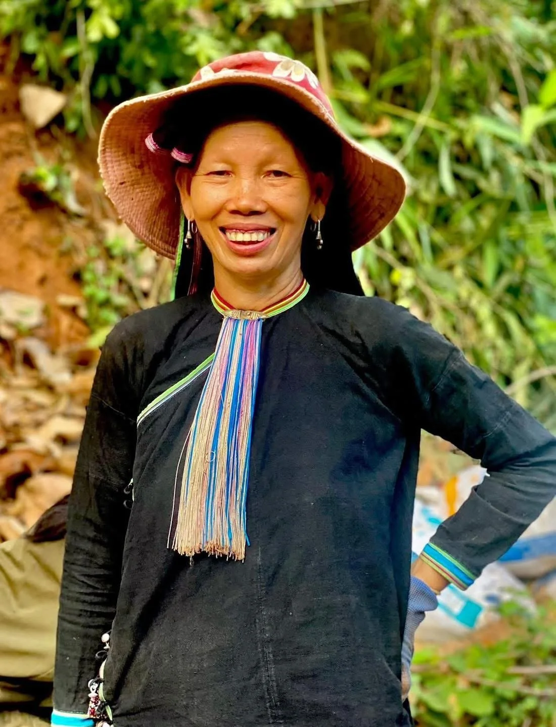 A Lan Tien woman smiling while wearing traditional clothing and a sun hat in the countryside of Dien Bien Phu