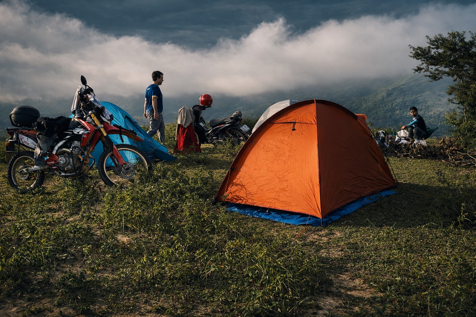 Travellers camping beside their motorbikes in the mountains of northern Vietnam at sunset.