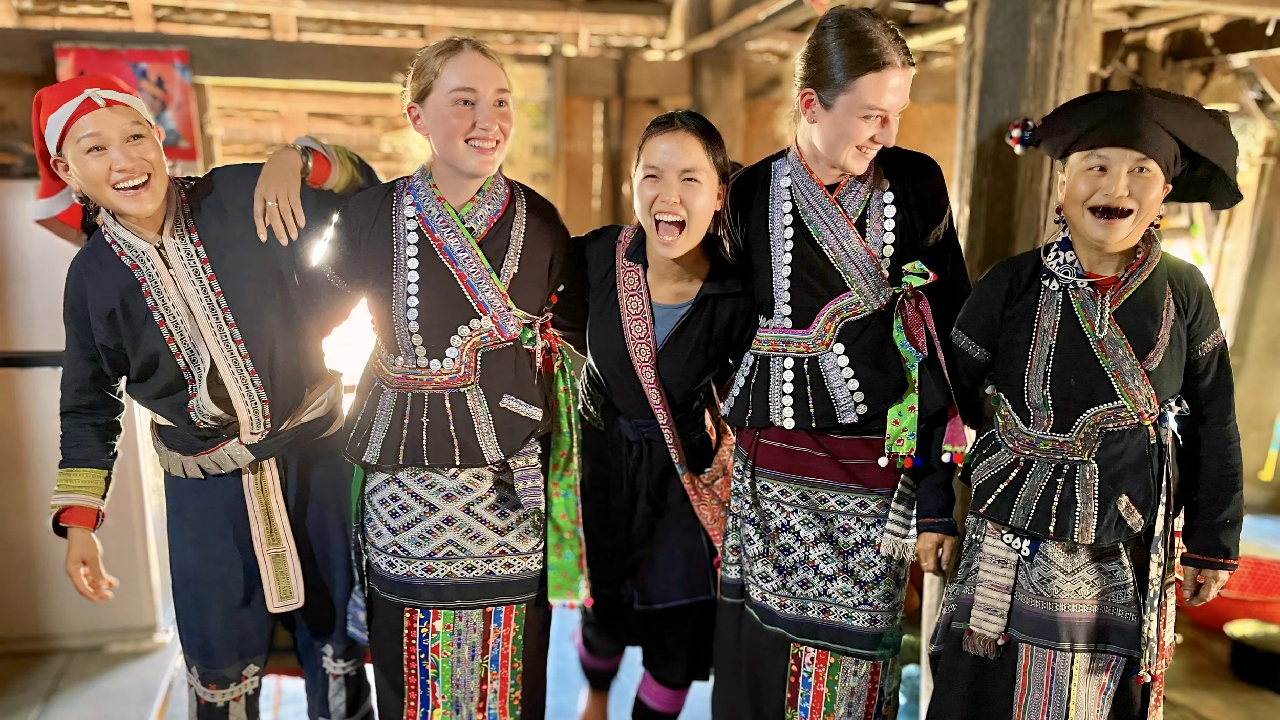 International guests with ETHOS Hmong and Dao women guides inside a traditional Lao ethnic home in Northern Vietnam.