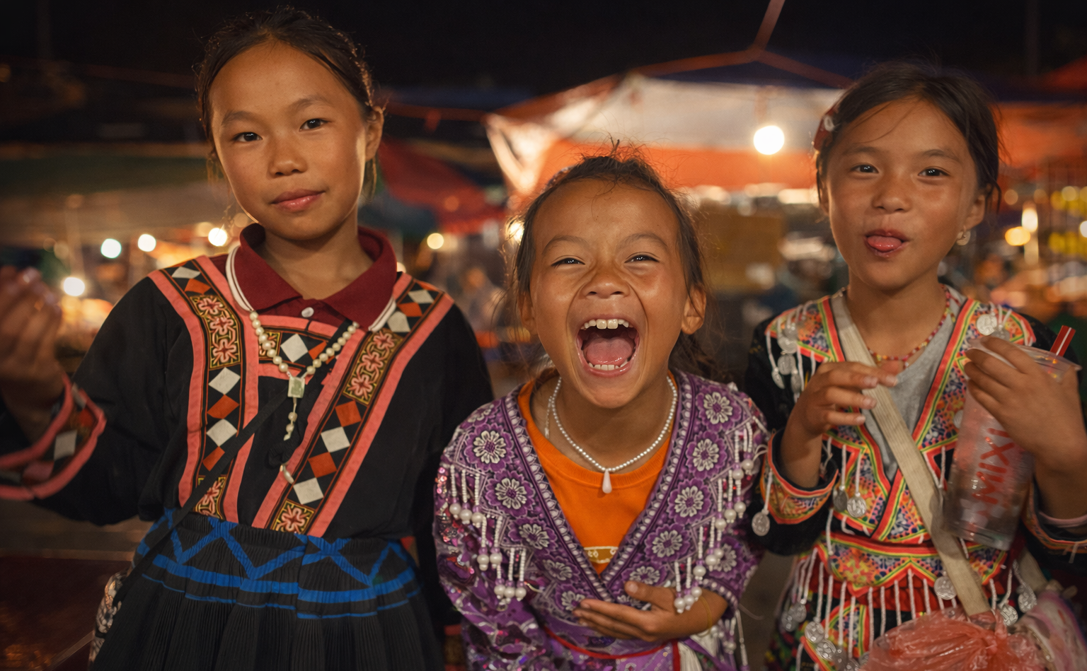 Young Hmong street sellers sharing a moment with visitors in central Sapa during the evening tourism crowds in 2025.
